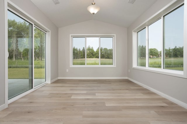 spare room featuring lofted ceiling, light hardwood / wood-style floors, and a healthy amount of sunlight