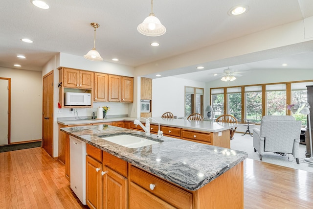 kitchen with a kitchen island with sink, light hardwood / wood-style floors, vaulted ceiling, pendant lighting, and white appliances