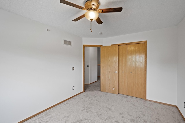 unfurnished bedroom with ceiling fan, a closet, light carpet, and a textured ceiling