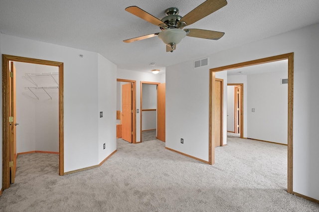 unfurnished bedroom featuring a spacious closet, a closet, light colored carpet, and ceiling fan