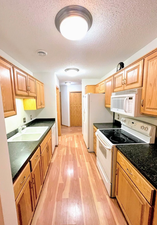 kitchen with light wood-type flooring, a textured ceiling, sink, and white appliances