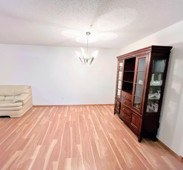 unfurnished room featuring a textured ceiling, an inviting chandelier, and light hardwood / wood-style flooring