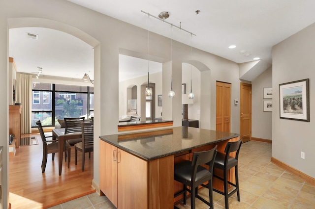 kitchen featuring dark stone countertops, track lighting, decorative light fixtures, and light wood-type flooring