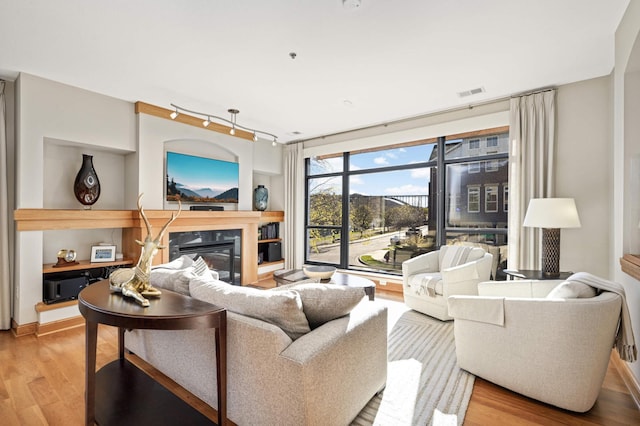 living room featuring built in features, light hardwood / wood-style floors, and track lighting