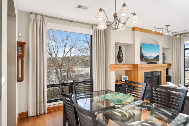 dining room with visible vents, wood finished floors, an inviting chandelier, and a glass covered fireplace