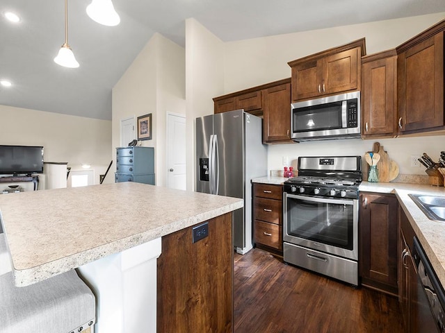 kitchen with stainless steel appliances, dark wood-type flooring, hanging light fixtures, vaulted ceiling, and a kitchen breakfast bar