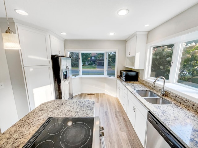 kitchen featuring light stone countertops, appliances with stainless steel finishes, sink, decorative light fixtures, and white cabinetry