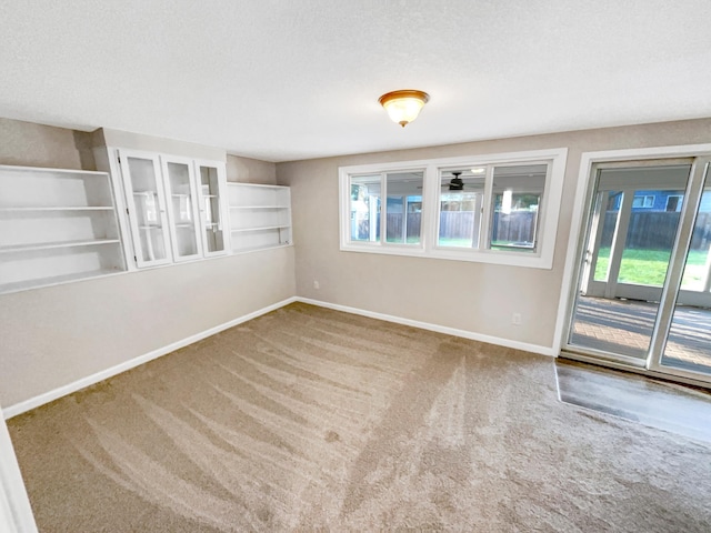 carpeted spare room featuring built in shelves, plenty of natural light, and a textured ceiling