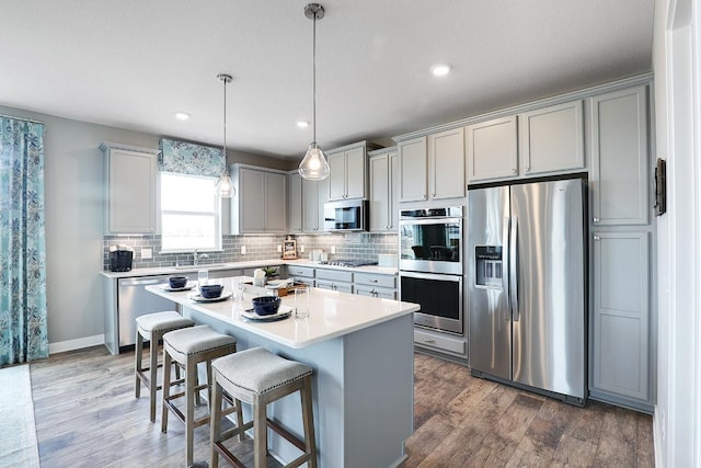 kitchen with a kitchen island, decorative light fixtures, hardwood / wood-style flooring, stainless steel appliances, and a breakfast bar