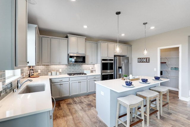 kitchen featuring sink, decorative light fixtures, stainless steel appliances, a center island, and light wood-type flooring