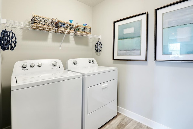 clothes washing area with washing machine and clothes dryer and light hardwood / wood-style flooring