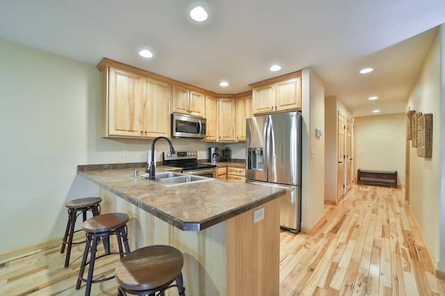 kitchen with light wood-type flooring, sink, kitchen peninsula, light brown cabinets, and appliances with stainless steel finishes