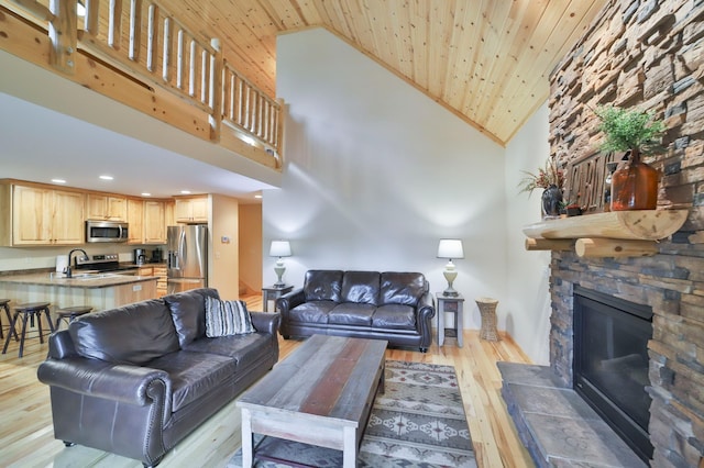 living room with high vaulted ceiling, wood ceiling, light hardwood / wood-style flooring, and a stone fireplace