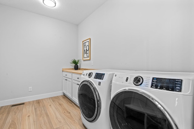 laundry room featuring light wood-type flooring, a textured ceiling, cabinets, and independent washer and dryer