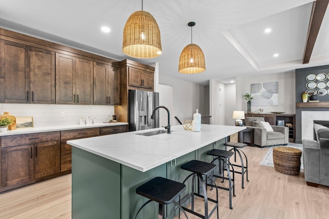 kitchen with a kitchen island with sink, light hardwood / wood-style flooring, stainless steel refrigerator with ice dispenser, and hanging light fixtures