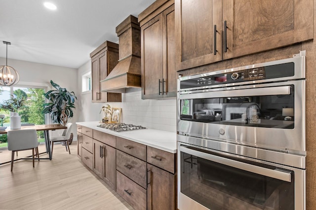 kitchen with light wood-type flooring, pendant lighting, a notable chandelier, stainless steel appliances, and premium range hood