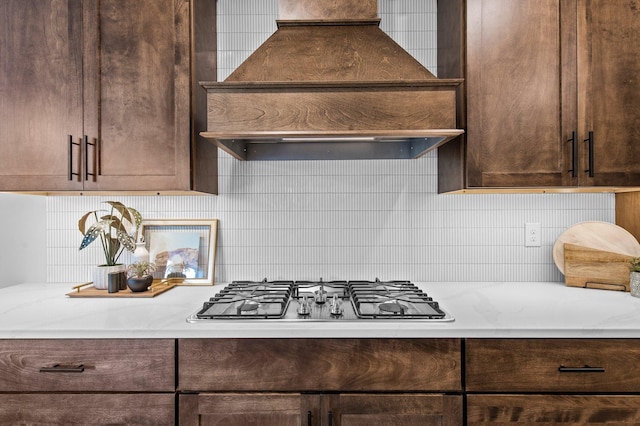 kitchen with dark brown cabinetry, stainless steel gas stovetop, custom exhaust hood, and tasteful backsplash