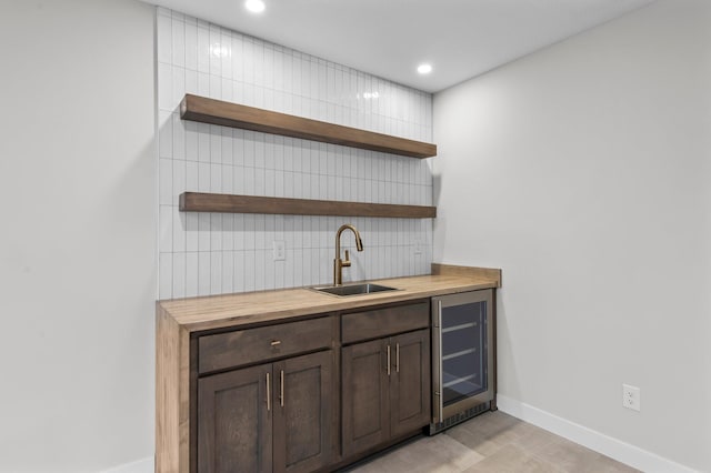 bar featuring wine cooler, butcher block countertops, sink, decorative backsplash, and dark brown cabinetry