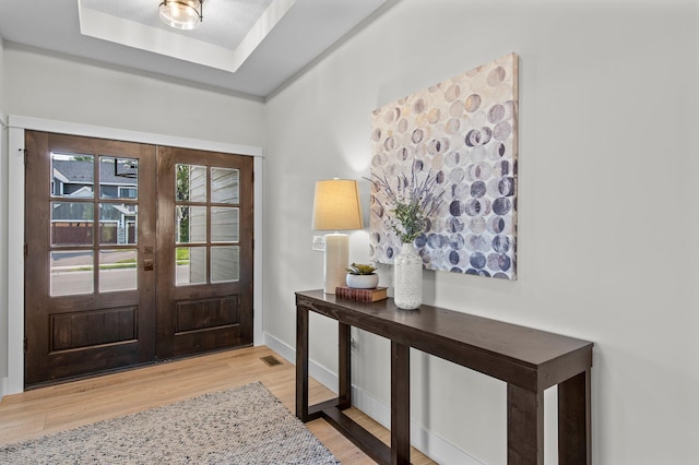 entrance foyer with baseboards, visible vents, a raised ceiling, wood finished floors, and french doors