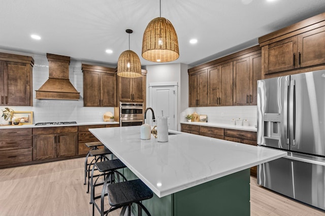 kitchen featuring stainless steel appliances, tasteful backsplash, custom range hood, a sink, and a kitchen breakfast bar