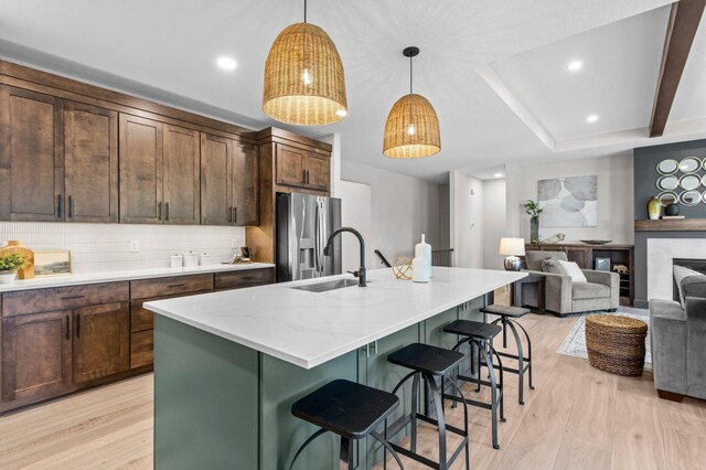 kitchen with light wood-type flooring, backsplash, a sink, and stainless steel refrigerator with ice dispenser