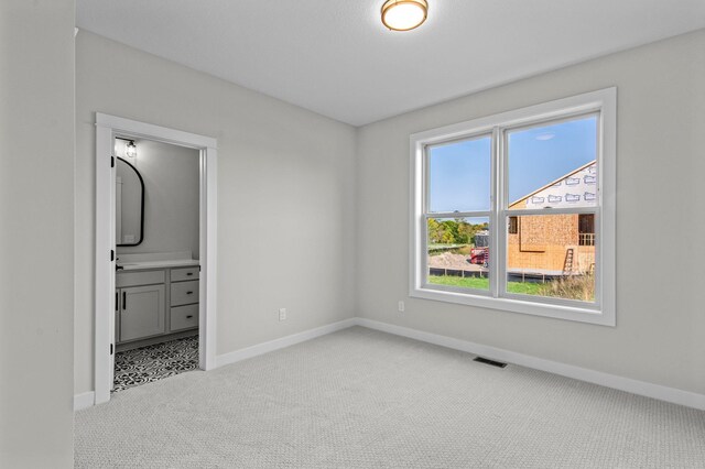 unfurnished bedroom with ensuite bath, baseboards, visible vents, and carpet flooring