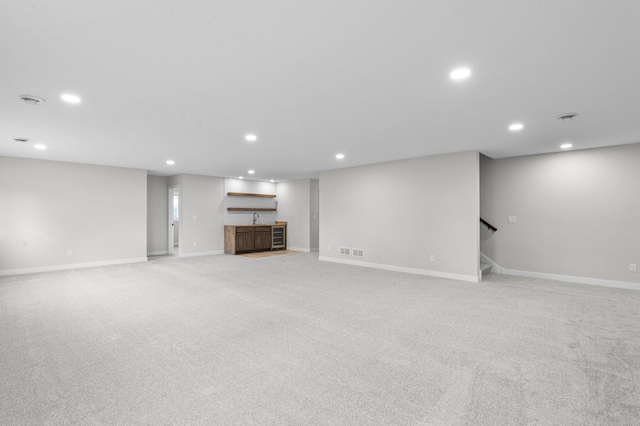 unfurnished living room with recessed lighting, light carpet, visible vents, stairway, and indoor wet bar