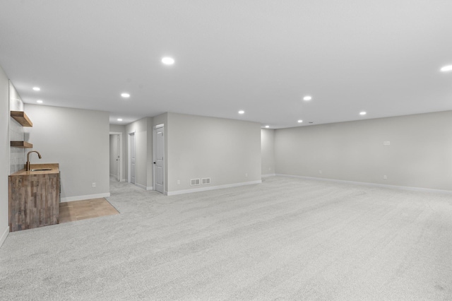 below grade area featuring light colored carpet, recessed lighting, visible vents, and a sink