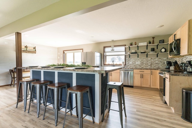 kitchen featuring light brown cabinetry, backsplash, a center island, appliances with stainless steel finishes, and a breakfast bar area