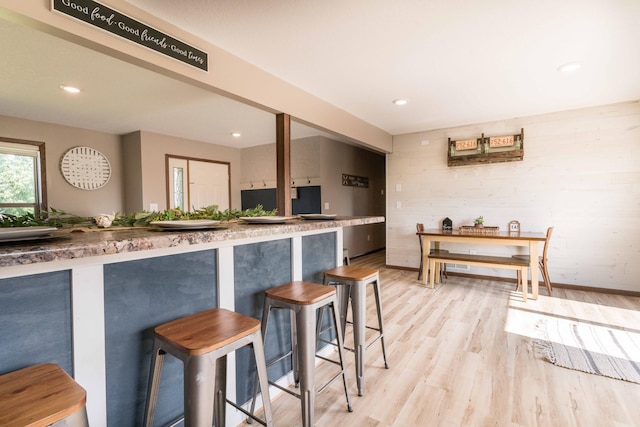 kitchen with recessed lighting, a kitchen breakfast bar, wood walls, and light wood finished floors