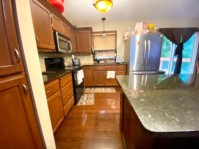 kitchen featuring dark stone countertops, hanging light fixtures, appliances with stainless steel finishes, dark wood-type flooring, and decorative backsplash