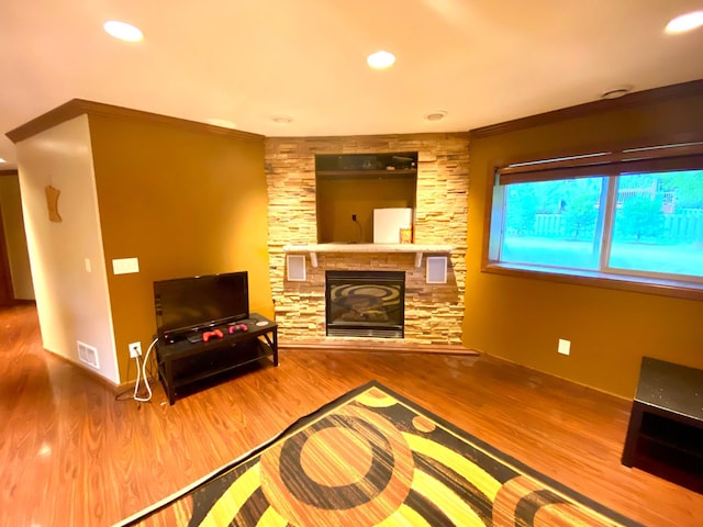 living room with crown molding, hardwood / wood-style floors, and a stone fireplace