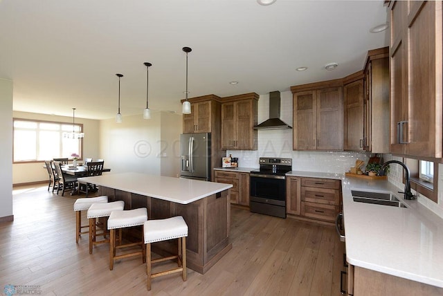 kitchen with a sink, a breakfast bar area, wall chimney exhaust hood, stainless steel appliances, and decorative backsplash