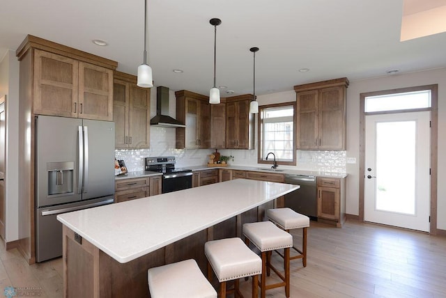 kitchen with appliances with stainless steel finishes, light hardwood / wood-style floors, wall chimney range hood, a kitchen island, and tasteful backsplash