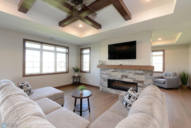 living room featuring light wood-type flooring, coffered ceiling, a stone fireplace, ceiling fan, and beam ceiling