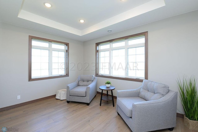 living area featuring recessed lighting, a tray ceiling, baseboards, and light wood-style floors