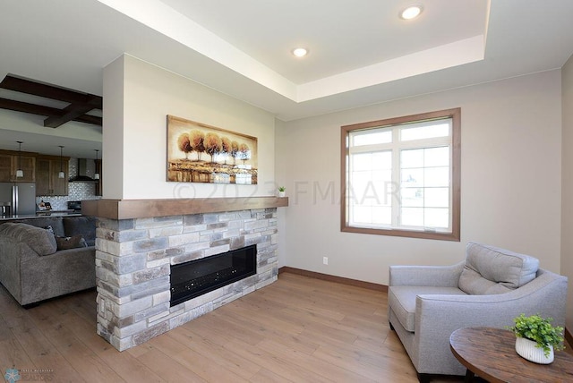 living room featuring beamed ceiling, a stone fireplace, and light wood-type flooring