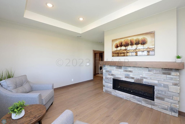 living area featuring a stone fireplace, baseboards, a raised ceiling, washer / dryer, and light wood-style floors