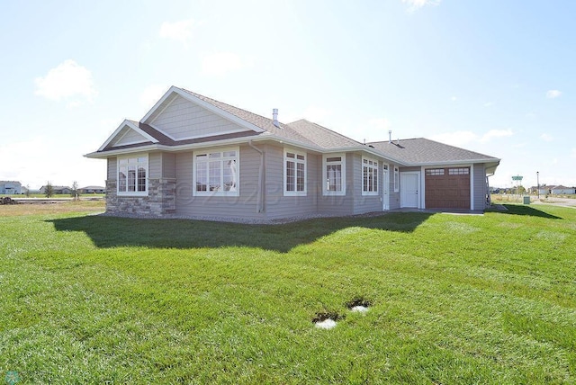 back of house with a yard, stone siding, and a garage