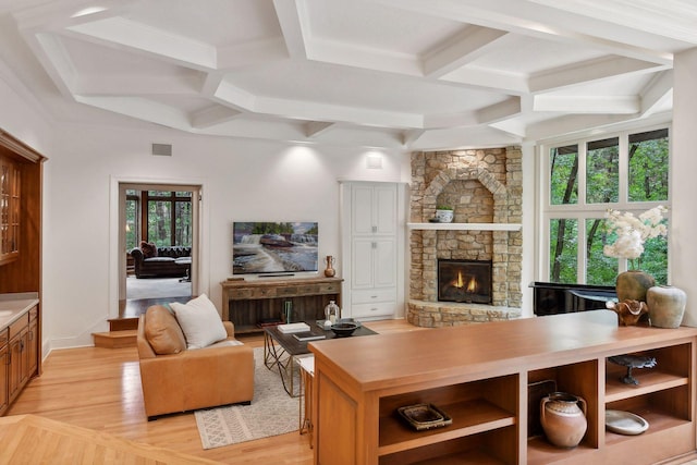 living room featuring a stone fireplace, light hardwood / wood-style flooring, beamed ceiling, and coffered ceiling