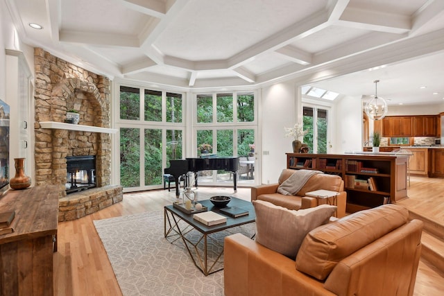 living room featuring coffered ceiling, beam ceiling, an inviting chandelier, light hardwood / wood-style flooring, and a stone fireplace