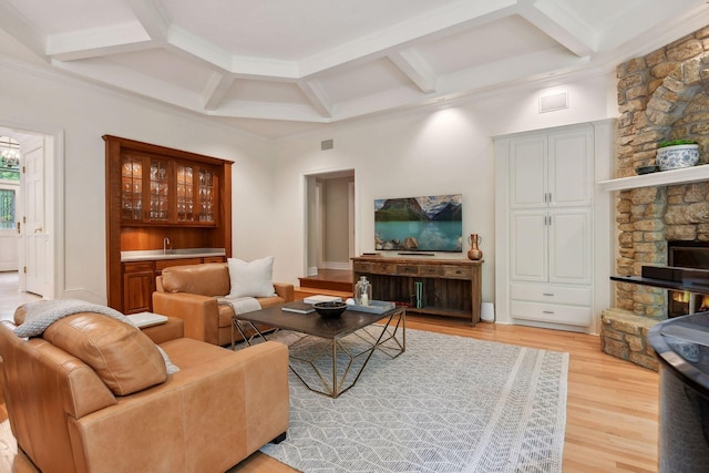 living room featuring bar area, light hardwood / wood-style flooring, a stone fireplace, and coffered ceiling