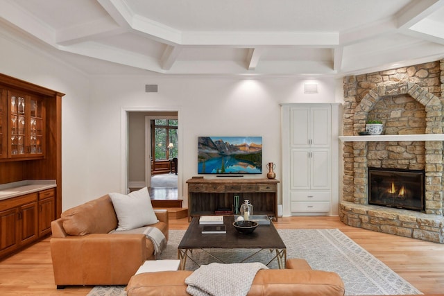 living room featuring beam ceiling, a stone fireplace, crown molding, and light hardwood / wood-style flooring