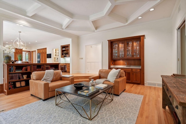 living room with light wood-type flooring, coffered ceiling, crown molding, an inviting chandelier, and beamed ceiling