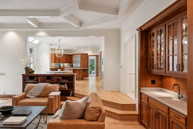 living room with coffered ceiling, sink, light hardwood / wood-style flooring, ornamental molding, and beam ceiling