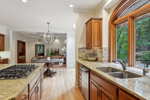 kitchen with sink, light stone countertops, light wood-type flooring, appliances with stainless steel finishes, and decorative light fixtures