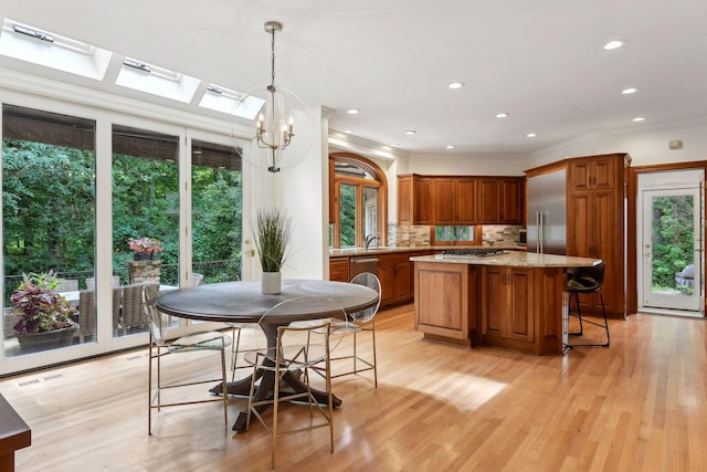 kitchen featuring an inviting chandelier, hanging light fixtures, a skylight, tasteful backsplash, and light stone counters