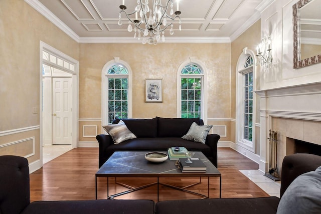 living room featuring a notable chandelier, light wood-type flooring, ornamental molding, and a tiled fireplace