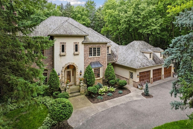 french country style house with a garage, stucco siding, brick siding, and aphalt driveway