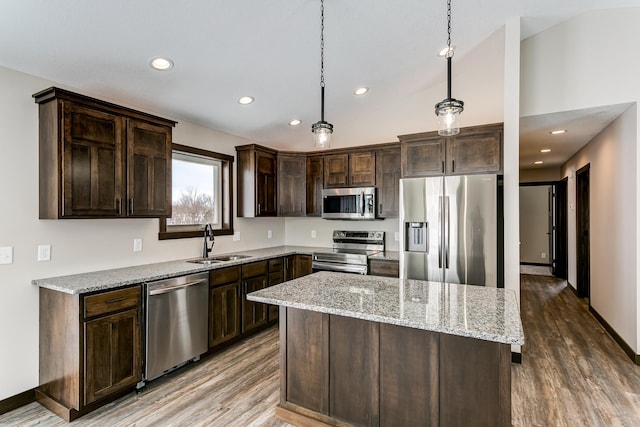 kitchen with lofted ceiling, hanging light fixtures, sink, a kitchen island, and appliances with stainless steel finishes